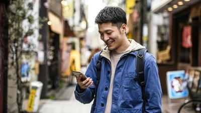 Cheerful young man looking at smartphone in street