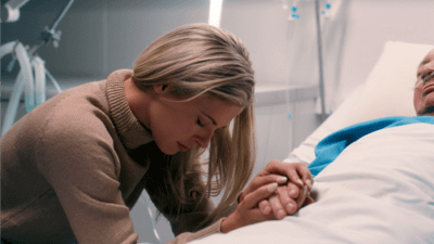 A woman holding a patients hand looking sad 