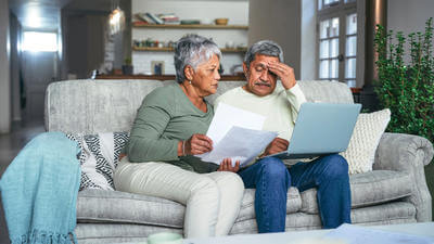 Older couple on sofa on laptop looking confused or stressed 