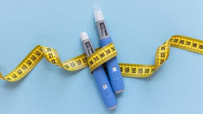Two injectors dosing pens for subcutaneous injection of antidiabetic medication or anti-obesity medication hovering over a blue background