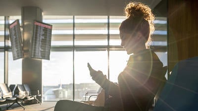 Female traveler texting on her phone while waiting by the gate at the airport