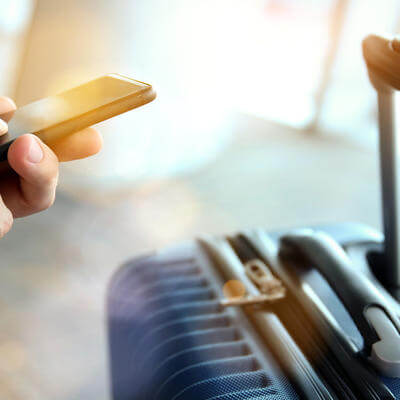 Image of a passenger on their phone with suitcase in the background