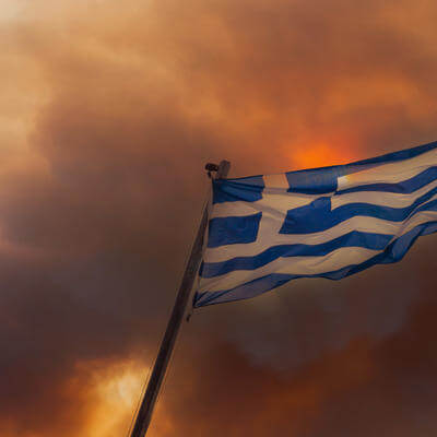Image of smoke and fire behind Greek flag