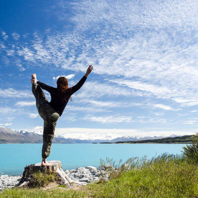 Woman doing yoga looking towards lake Pukaki and Mount Cook on a sunny day 