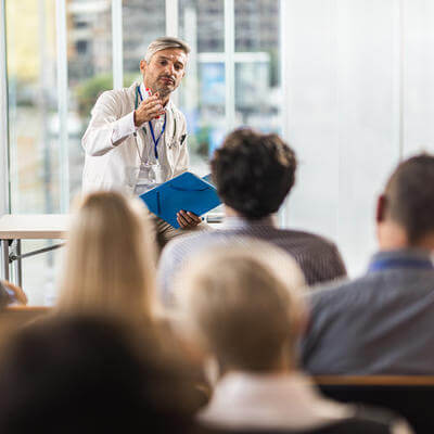 Male doctor talking to large group of people on a seminar in a board room