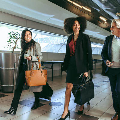 Group of business people going on business trip carrying suitcases while walking through airport passageway.