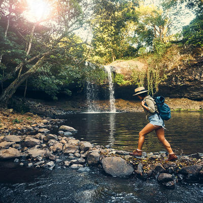 Shot of a young woman walking on a rocky surface towards a waterfall in the forest