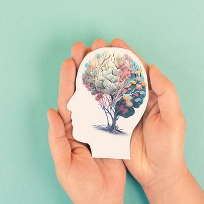 Hands holding paper head, human brain with flowers, self care and mental health concept, positive thinking, creative mind