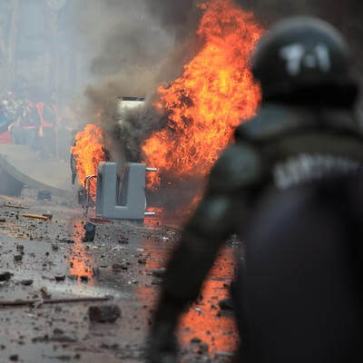 Riot police officer standing before a fire and a crowd of people