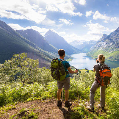 Two hikers at viewpoint in mountains with lake, sunny summer 