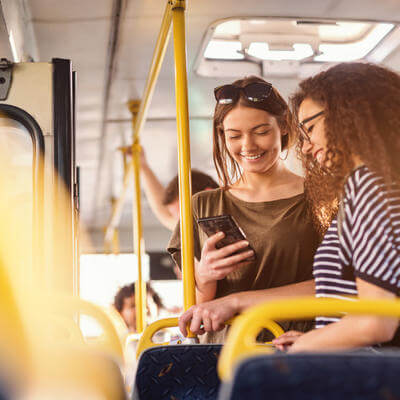 Two girls watching phone and smiling while standing on a bus
