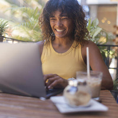 Smiling woman uses a laptop for remote work while sitting in a coffee shop drinking coffee 
