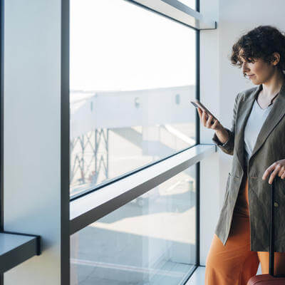 Female Standing At The Airport And Holding Her Luggage While Watching Something On Her Smartphone -