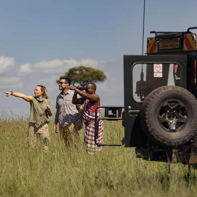 Couple of tourists and their guide looking in the distance in search of wild animals in nature reserve of Kenya