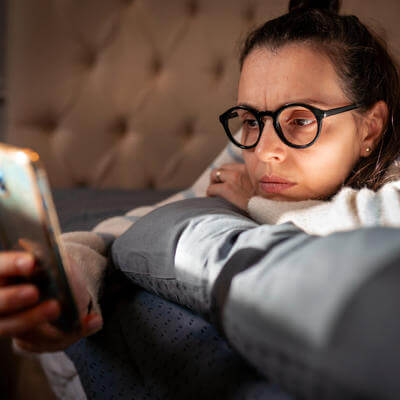 Woman on bed anxiously stares at phone 