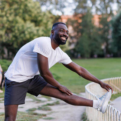 Happy man stretching leg on park fence after jog 