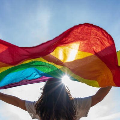 Picture of a young woman waving lgbtq flag under the sky