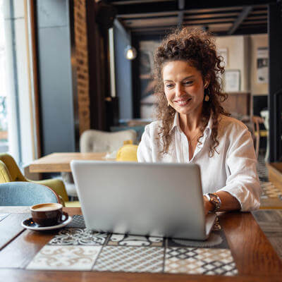 Freelancer working on laptop in coffee shop enjoying cappuccin