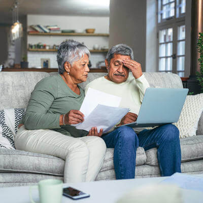 Older couple on sofa on laptop looking confused or stressed 