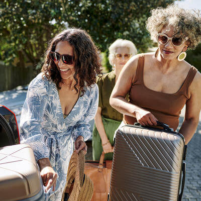 Smiling women packing bags into a car for a road trip together 