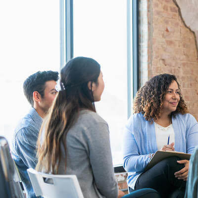 The diverse therapy group listens attentively as the young adult woman shares