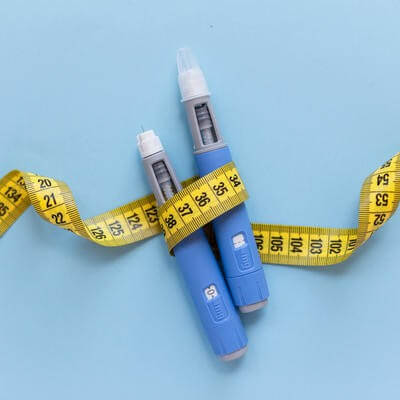 Two injectors dosing pens for subcutaneous injection of antidiabetic medication or anti-obesity medication hovering over a blue background