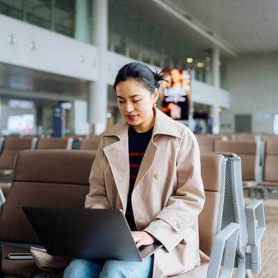 Asian businesswoman working on laptop while sitting at airport terminal waiting for her flight, a suitcase by her side