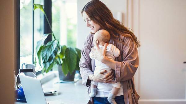 Mum holding baby looking at laptop