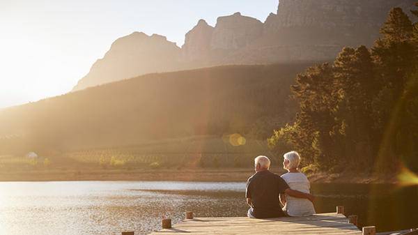 Mature couple sitting lakeside by mountains 