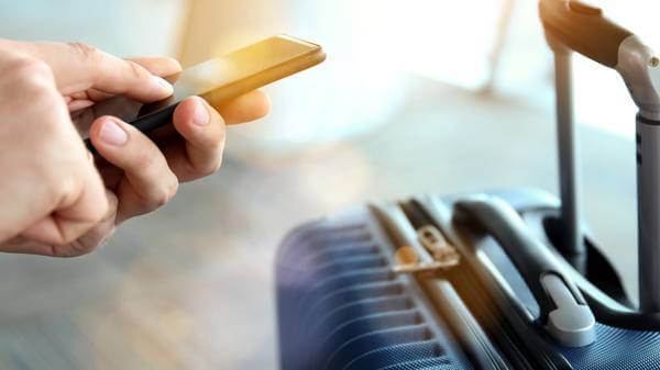 Image of a passenger on their phone with suitcase in the background
