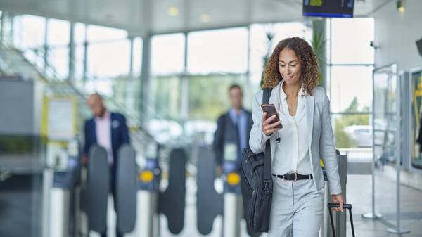 Image of a passenger on their phone with suitcase in the background
