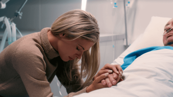 A woman holding a patients hand looking sad 