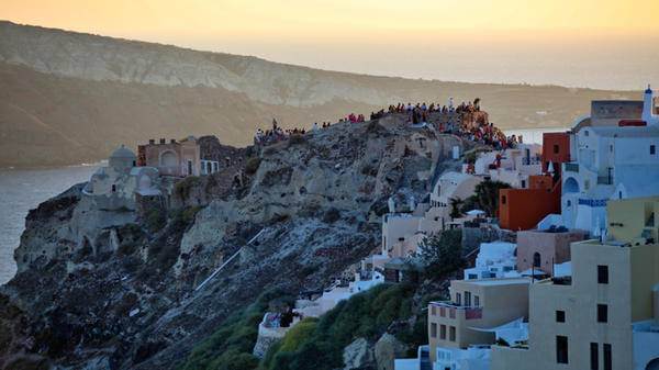 Tourists waiting to see the sunset from ancient fortress in Oia city, Santorini, Greece