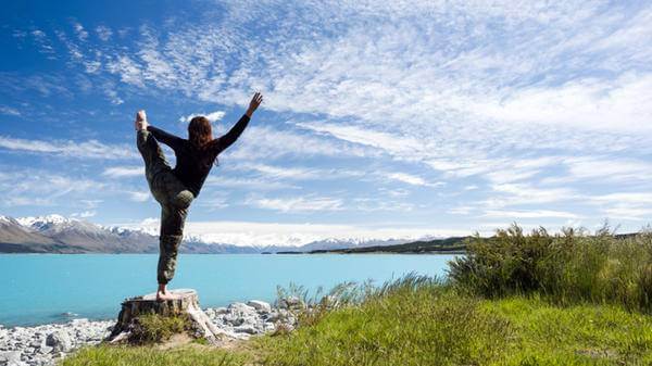 Woman doing yoga looking towards lake Pukaki and Mount Cook on a sunny day 