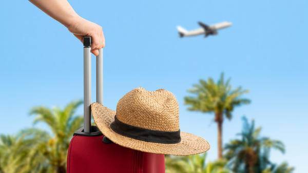 Woman with red suitcase standing on passengers ladder of airplane opposite sea with palm trees