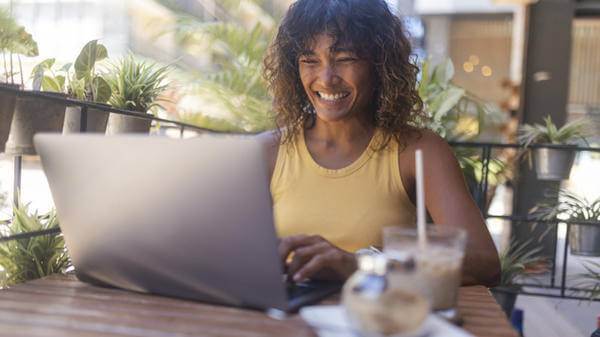 Smiling woman uses a laptop for remote work while sitting in a coffee shop drinking coffee 