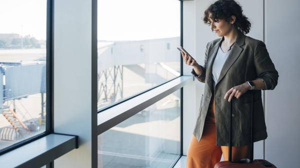 Female Standing At The Airport And Holding Her Luggage While Watching Something On Her Smartphone -