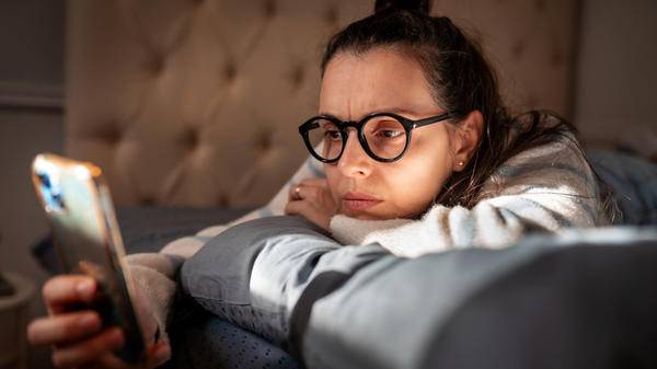 Woman on bed anxiously stares at phone 