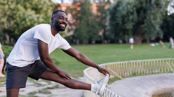 Happy man stretching leg on park fence after jog 