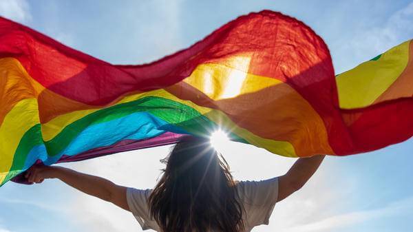 Picture of a young woman waving lgbtq flag under the sky