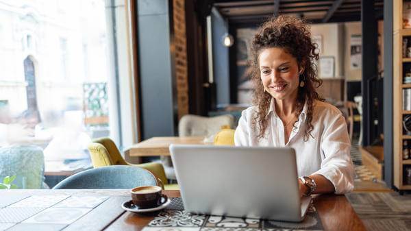 Freelancer working on laptop in coffee shop enjoying cappuccin