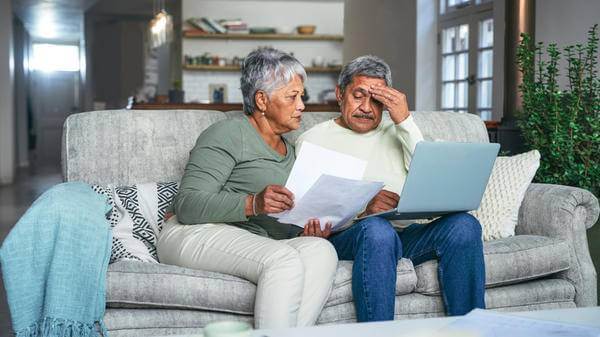 Older couple on sofa on laptop looking confused or stressed 