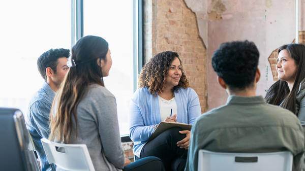 The diverse therapy group listens attentively as the young adult woman shares