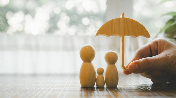 Parent and child model holding an umbrella on a wooden table, concept of health insurance, life and savings insurance