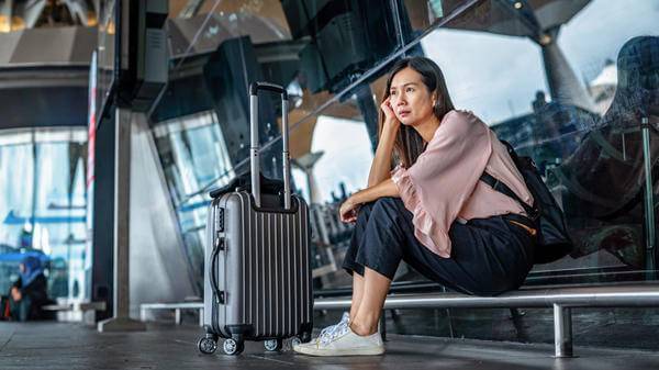 Lone female traveller sits at an airport looking fed up 