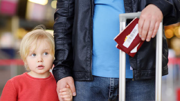 A child holds their parents hand who is holding two passports and a suitcase