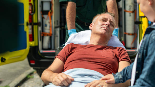 A father on a stretcher being taken to an ambulance by a paramedic