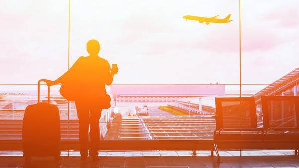 Woman looking out of an airport window, looking at a plane taking off