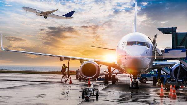 aeroplane parked with a plane in the background flying off 